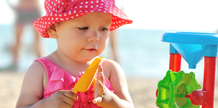 Lille pige med lyserød hat leger med sandmølle