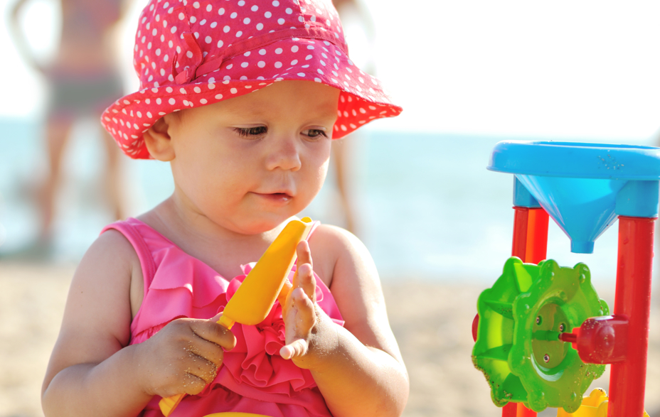 Lille pige med lyserød hat leger med sandmølle