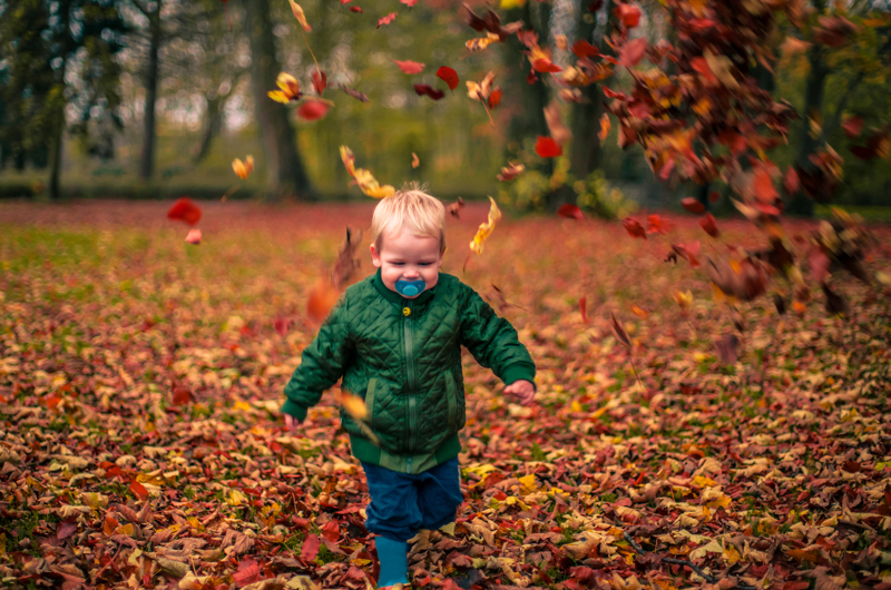 Barn i grøn flyverdragt som løber gennem bladene i skoven