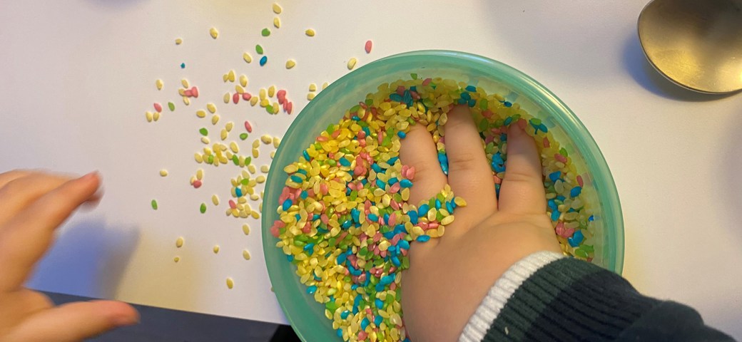 Barn dykker ned med hånden i en skål med farvede ris