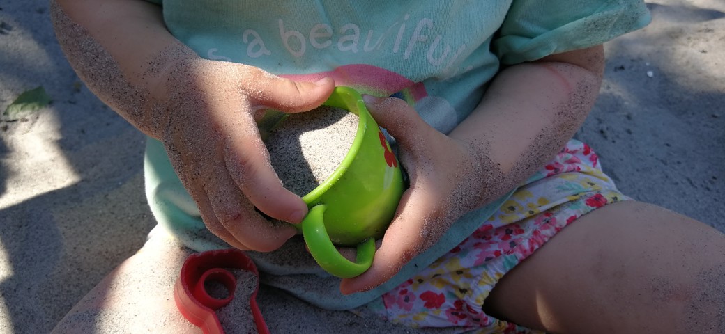 Barn sidder og leget i sandkasse med en grøn kop